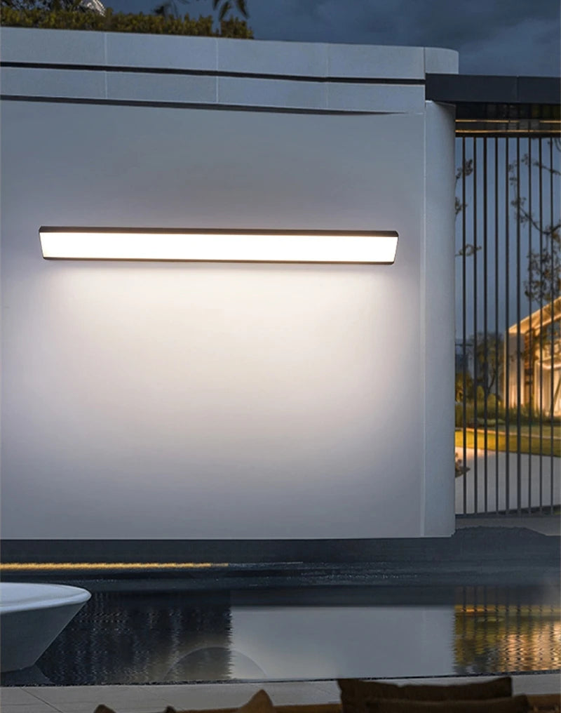 Modern outdoor wall light fixture on a building exterior with a pool and garden in the background.