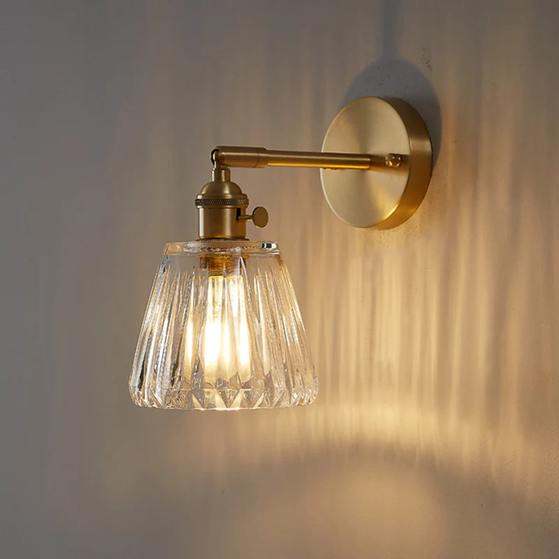 Wall-mounted light fixture with glass shade and brass arm on a wall.