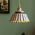 Striped pendant light with gold fixture against a green wall