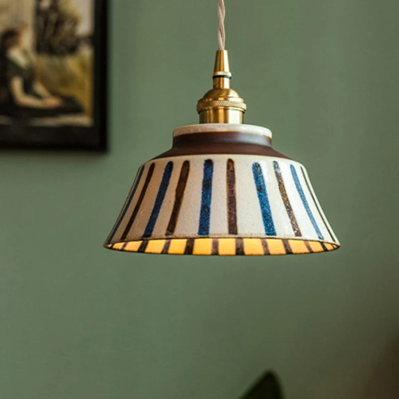 Striped pendant light with gold fixture against a green wall