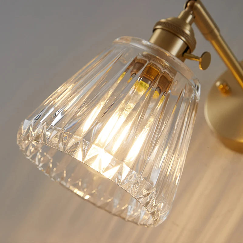 Close-up of a gold wall-mounted lamp with a clear glass shade on a neutral background