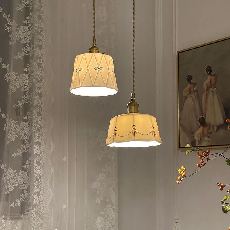 Two pendant lights hanging from a ceiling with a decorative wall and floral branch in the background.