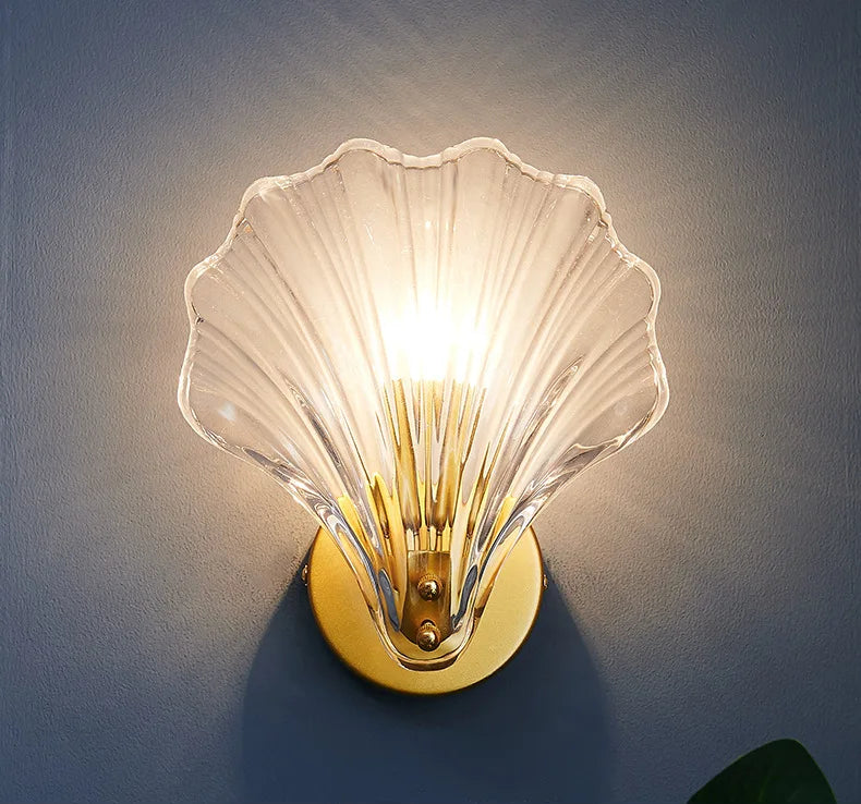 Shell-shaped wall sconce with clear glass shade on a dark background
