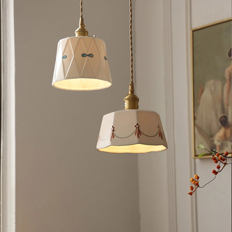 Two pendant lights hanging from a ceiling with a neutral wall and artwork in the background.