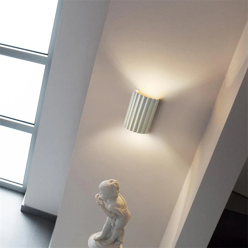 Wall-mounted light fixture on a white wall with a window in the background