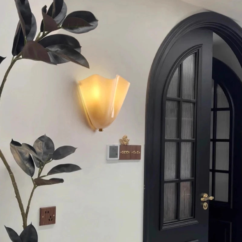 Decorative wall light fixture on a white wall with a black door and plant.