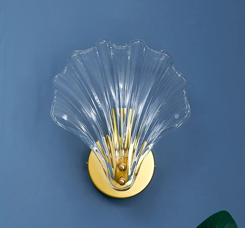 Decorative wall sconce with clear glass and gold metal base on a blue background