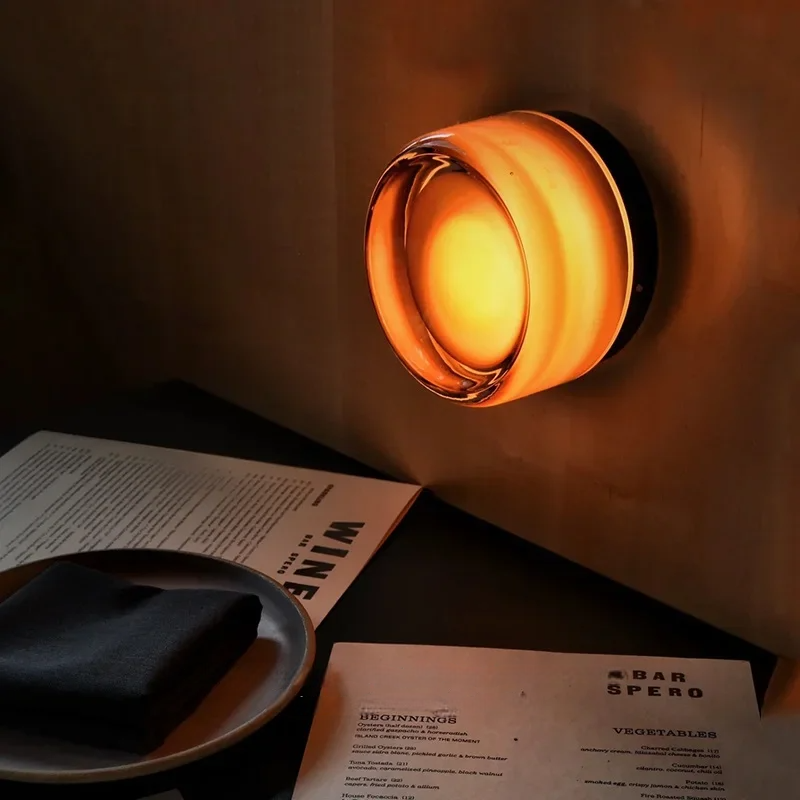 Amber glass wall sconce illuminating a table with a menu and napkin in a dimly lit setting