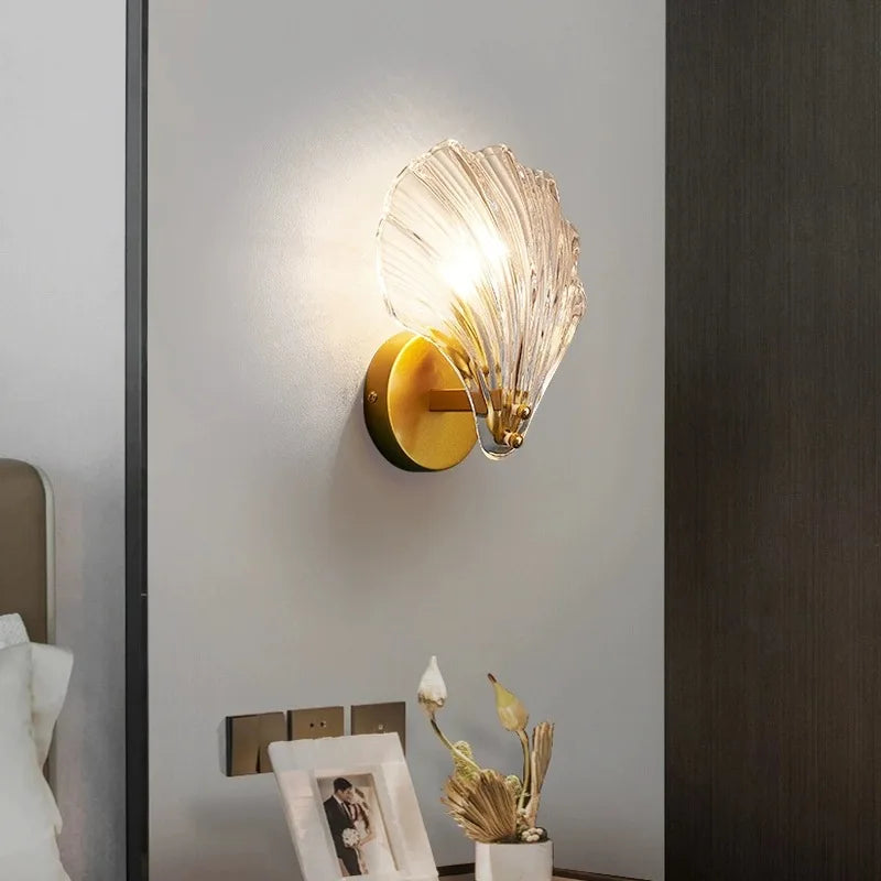 Glass wall sconce on a white wall next to a bed and illuminating over a bedside table