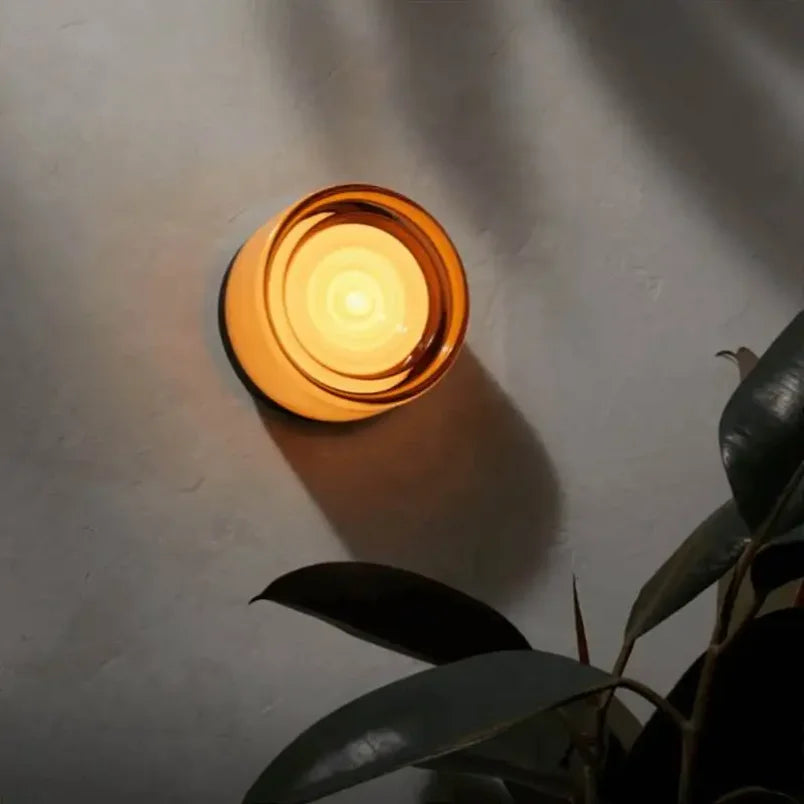 Round wall light fixture on a textured wall with a plant in the foreground