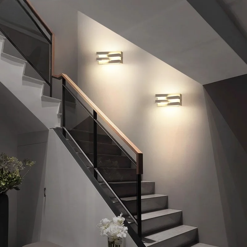 Modern staircase with wall lights and a vase of flowers on a gray wall.