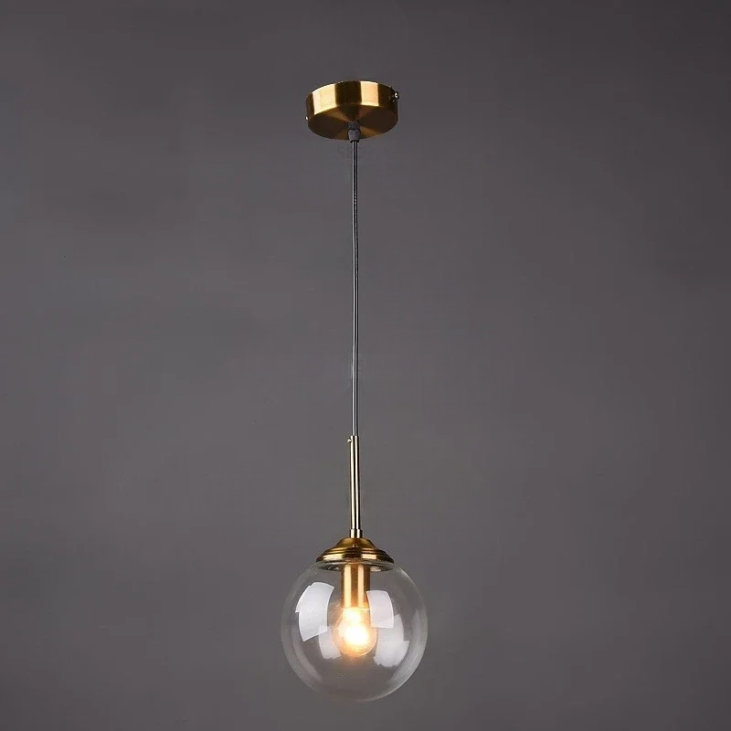 Transparent pendant light with gold fixture and clear glass shade on a dark background