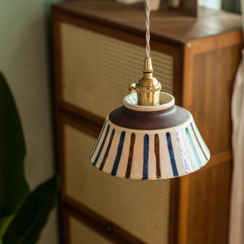 Decorative pendant light with striped shade hanging against a wooden cabinet.