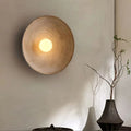 Ceramic wall light fixture on a neutral wall with a vase and branches in the foreground.