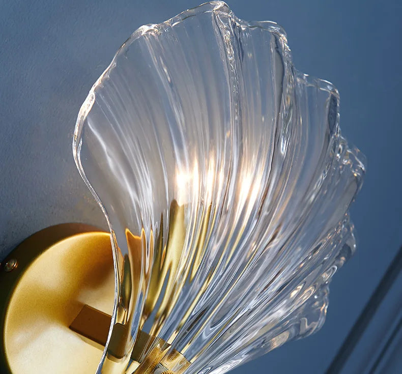 Decorative wall light fixture with clear glass shade against a blue background