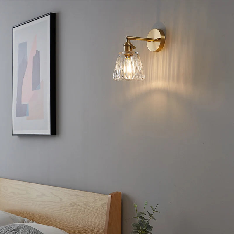 Wall-mounted lamp with glass shade on a grey wall above a bed.
