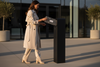 Woman in a trench coat using a black mailbox outdoors.